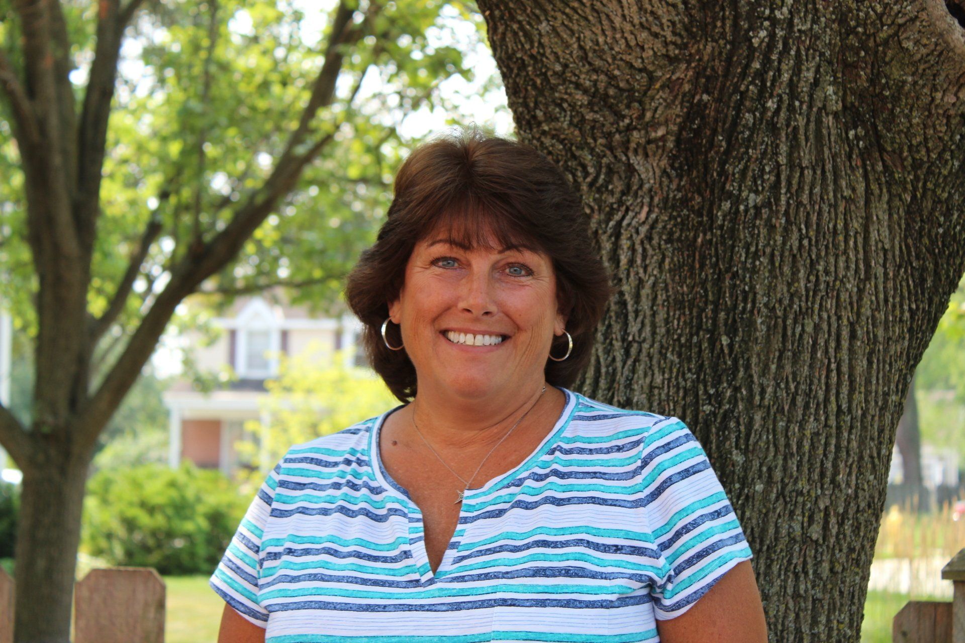 A woman in a striped shirt is smiling in front of a tree.