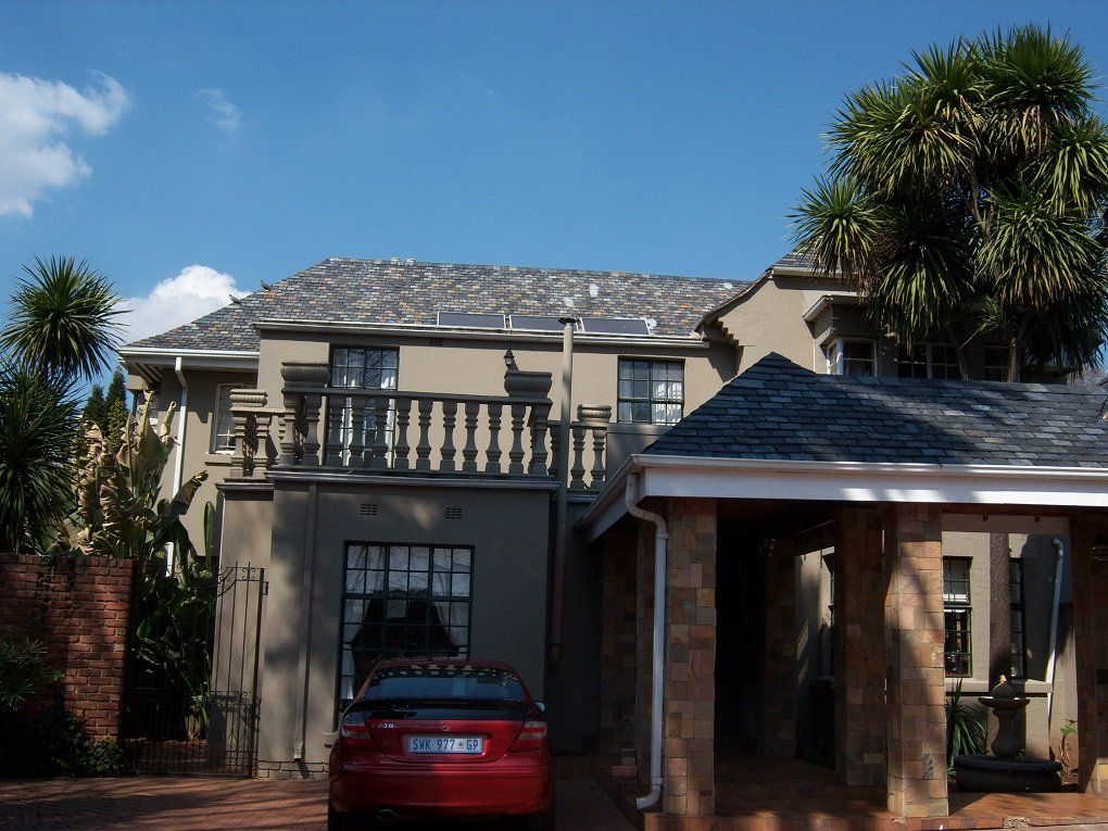 A red car is parked in front of a large house