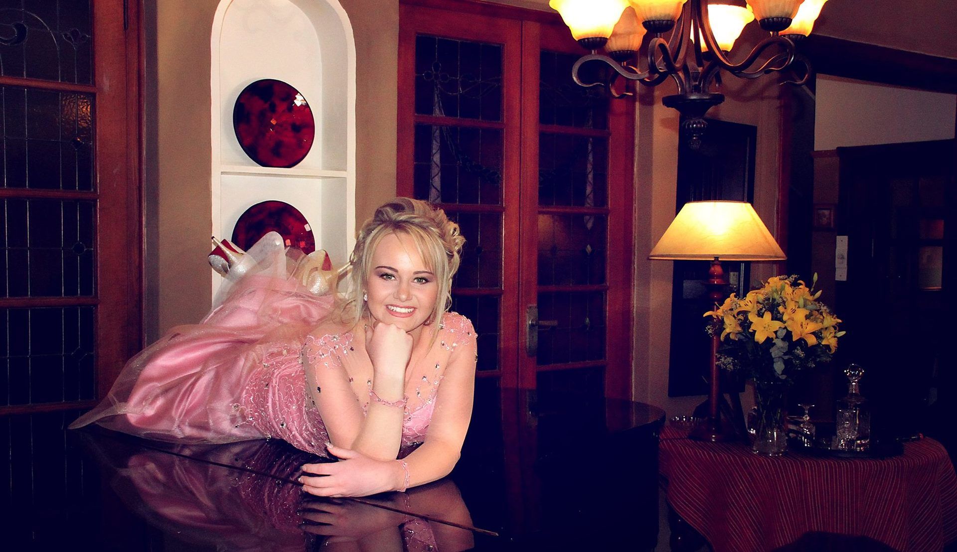 A woman in a pink dress is laying on a piano
