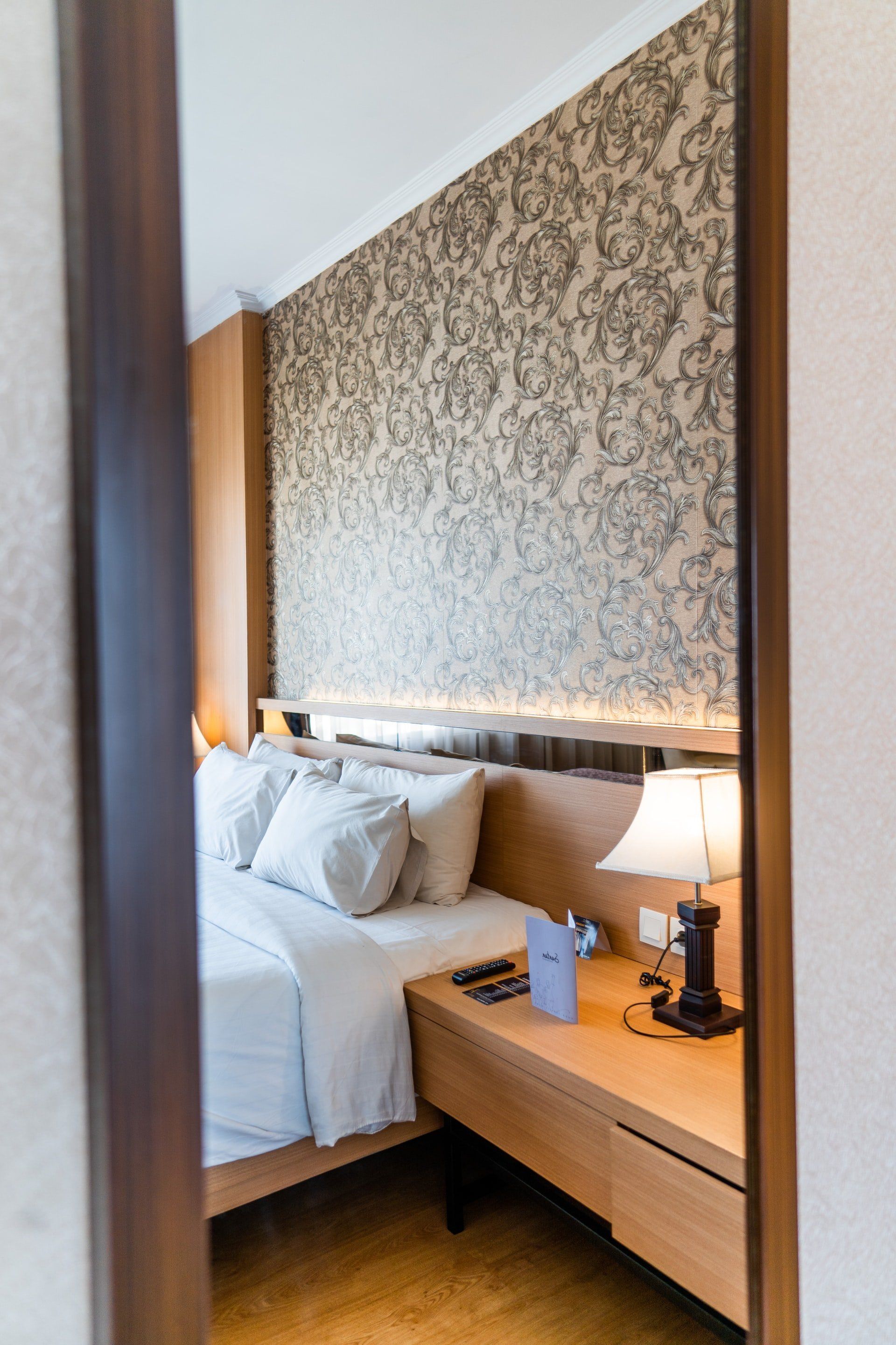 A bedroom with a bed , nightstand , lamp and mirror.
