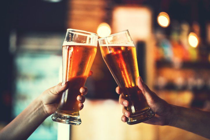 Two people toasting with glasses of beer in a bar, blurred background.