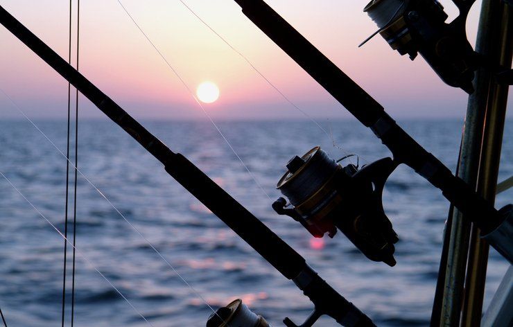 Fishing rods silhouetted against a sunset over the ocean.