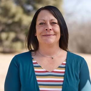 A woman wearing a striped shirt and a blue cardigan is smiling for the camera.