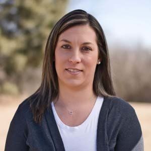A woman wearing a gray sweater and a white shirt is standing in a field.