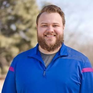 A man with a beard is wearing a blue jacket and smiling for the camera.
