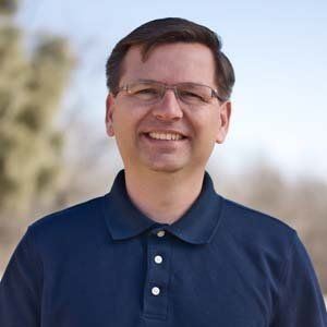 A man wearing glasses and a blue shirt is smiling for the camera.