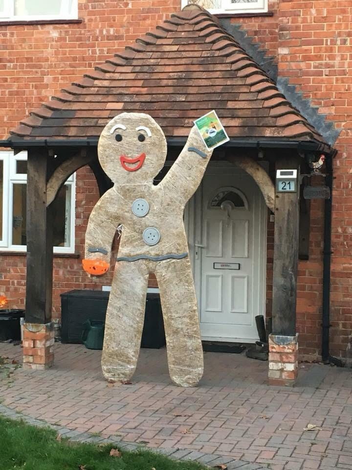 Giant gingerbread man decoration waving a book outside a brick house.
