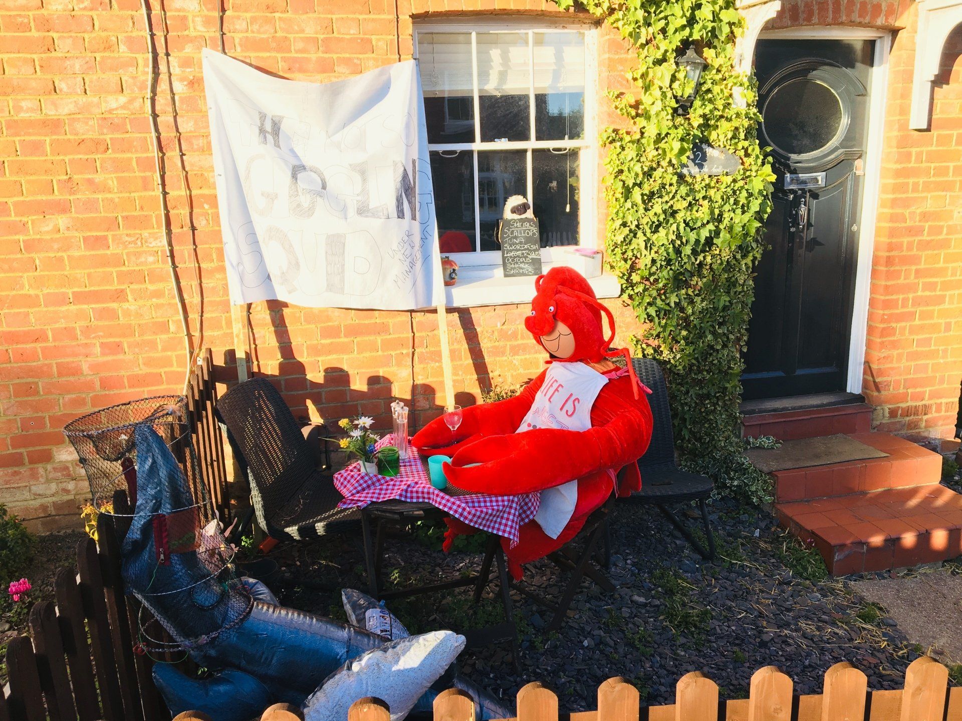 Red character figure sitting at a table outside a brick building.