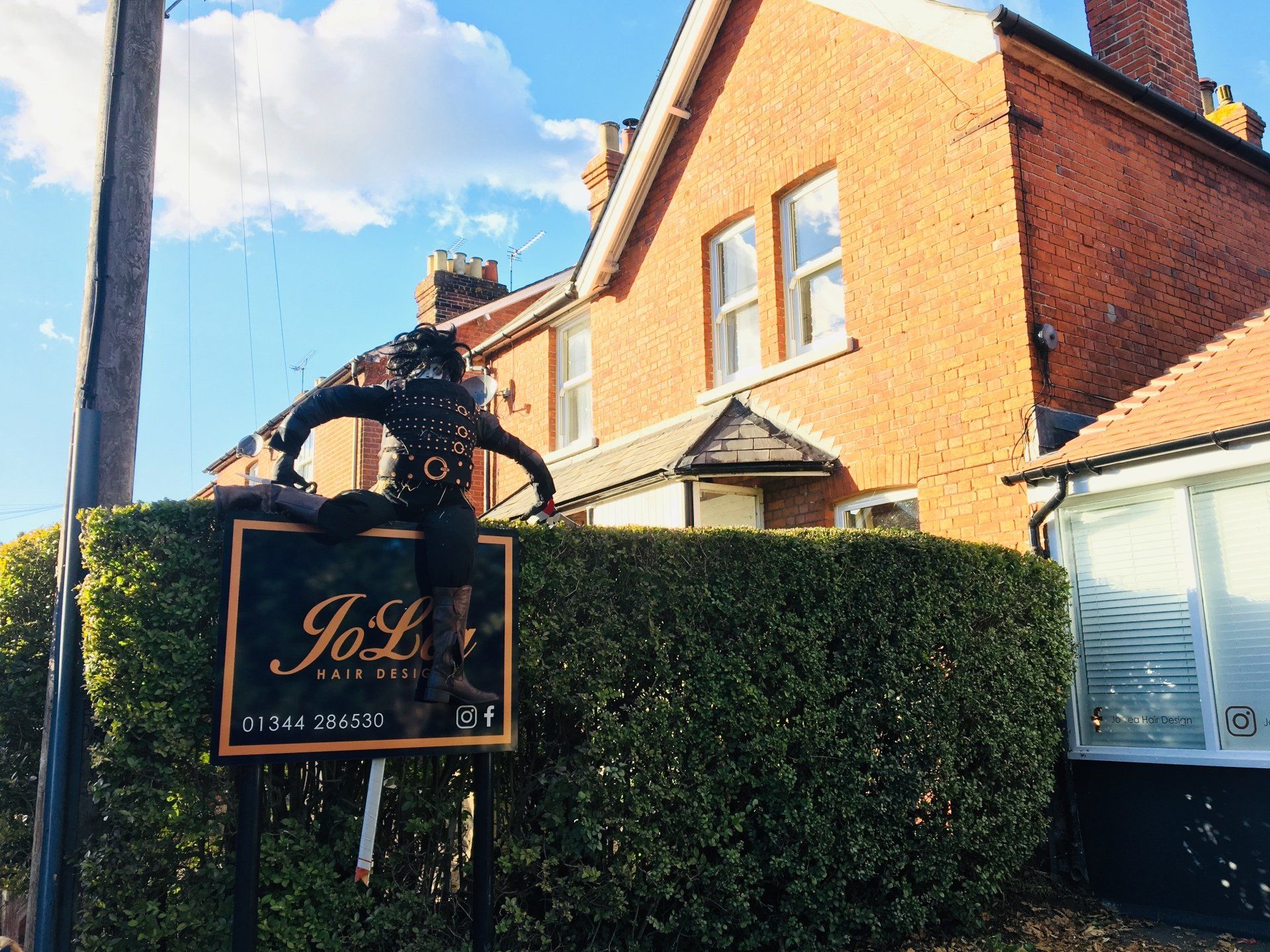Sign for Jo Lo's Hair Studio with a sculpture of a person on top, set in front of a brick building.