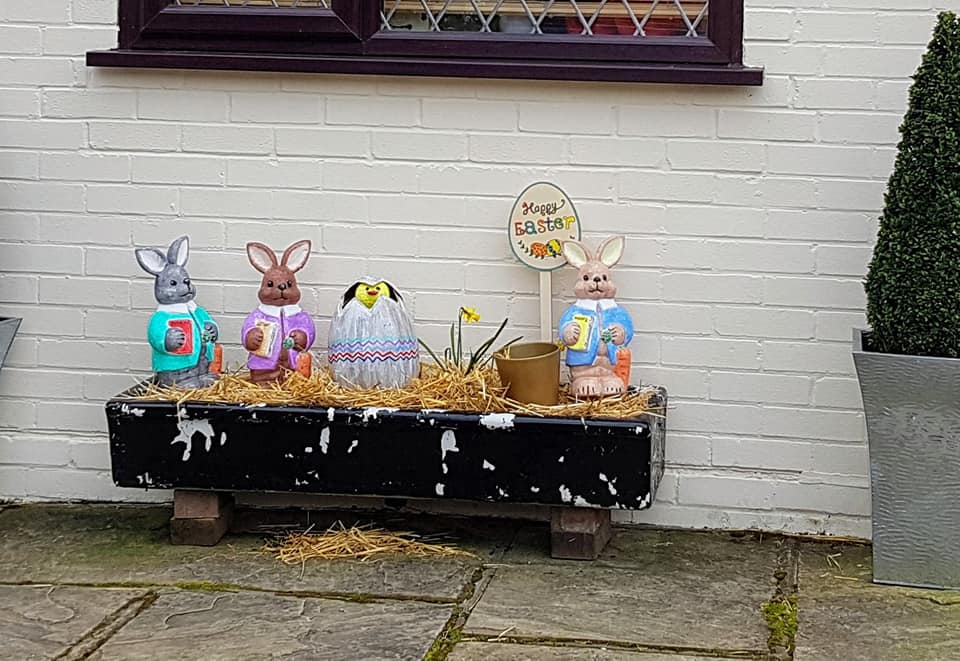 Easter bunny decorations in a black trough planter against a white brick wall.