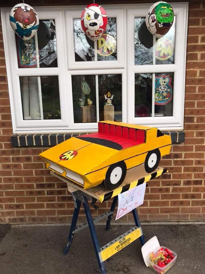 Yellow toy car on a sawhorse in front of a window decorated with character balloons.