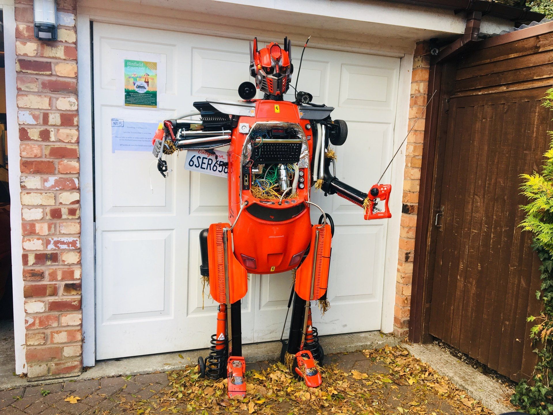 Orange robot standing in front of a white garage door, leaves on the ground.
