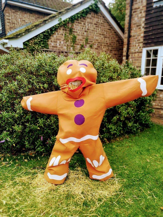 Gingerbread man costume with outstretched arms, purple buttons, and open mouth, standing on grass.