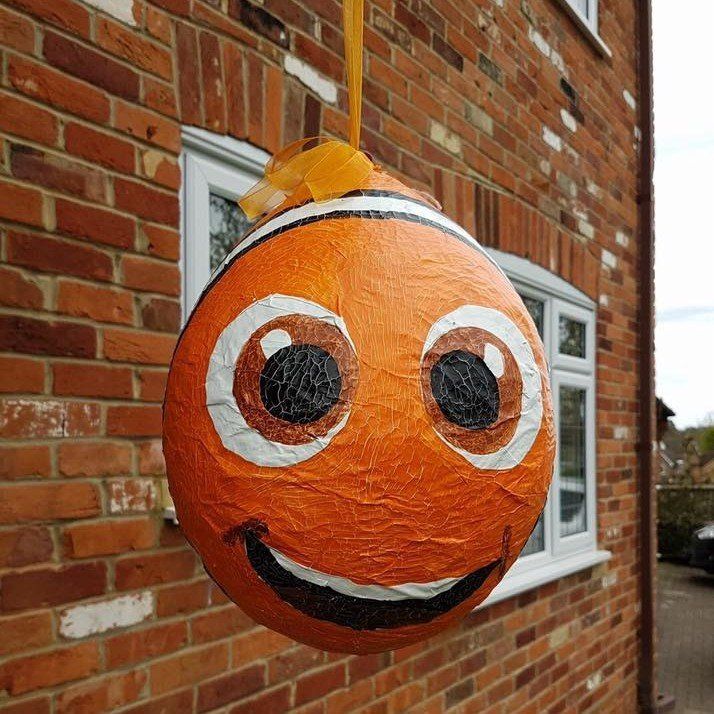 Orange, round Nemo decoration with a smiling face, hanging outside a brick building.