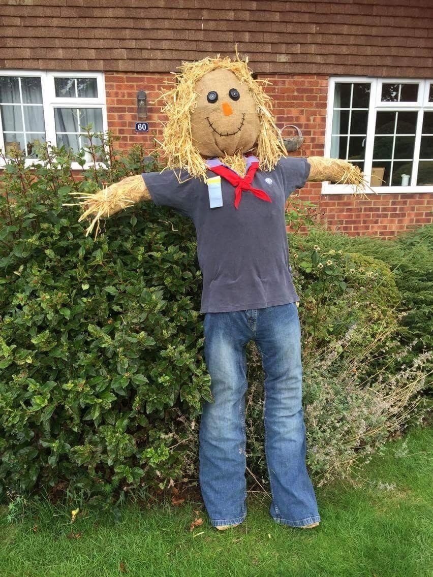 Scarecrow made of straw wearing a blue shirt, jeans, and a red scarf, standing in a garden.