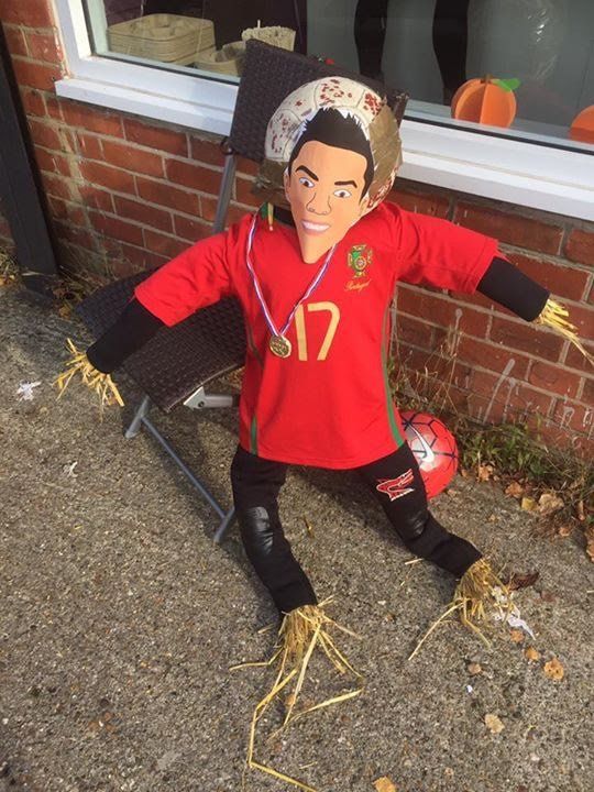 Scarecrow figure of a soccer player in a red jersey, sitting on a chair.