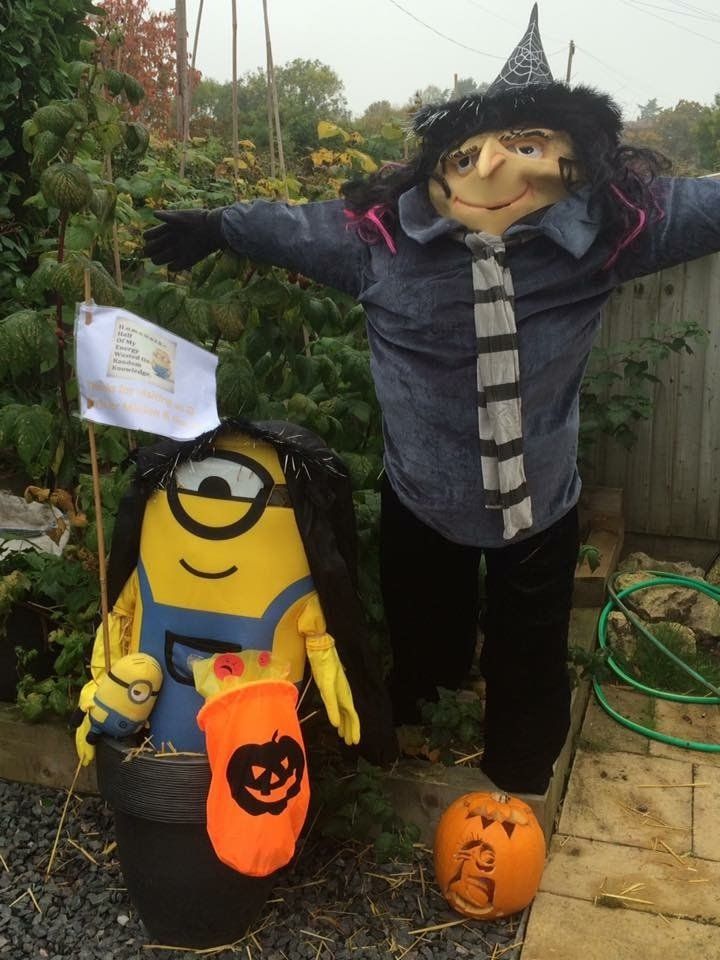 Two scarecrows: a witch and a minion, decorated for Halloween, standing next to a carved pumpkin.