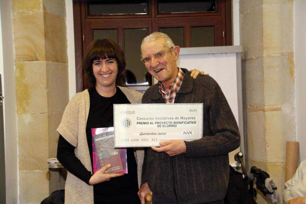 Mujer y hombre mayor sonriendo, sosteniendo un gran cheque en el interior.