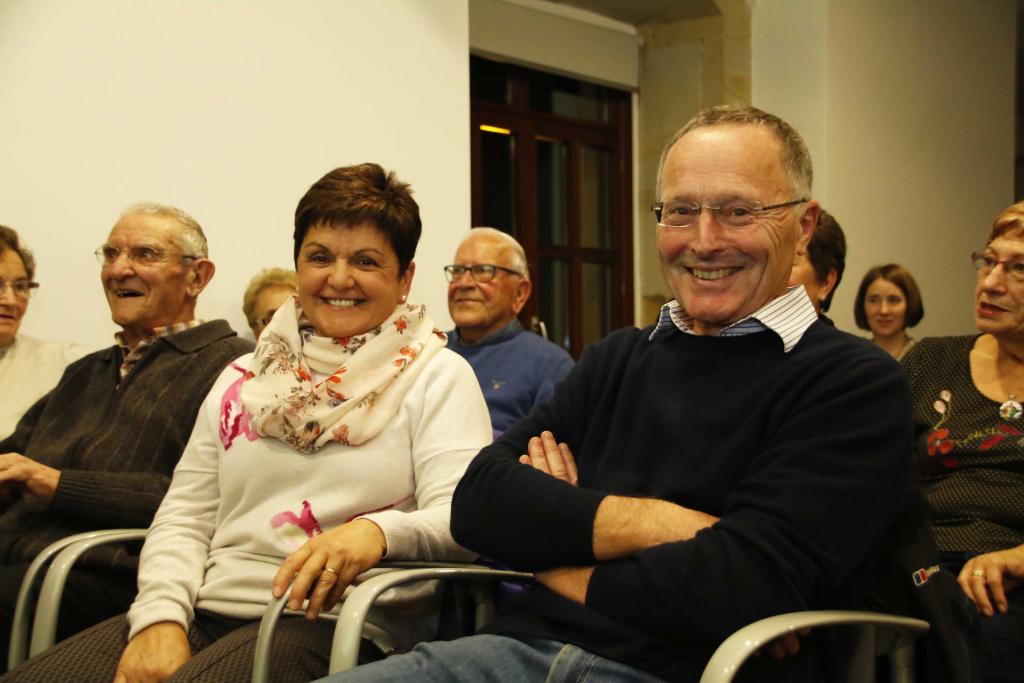 Personas mayores sonrientes sentadas en sillas, dentro de una habitación.