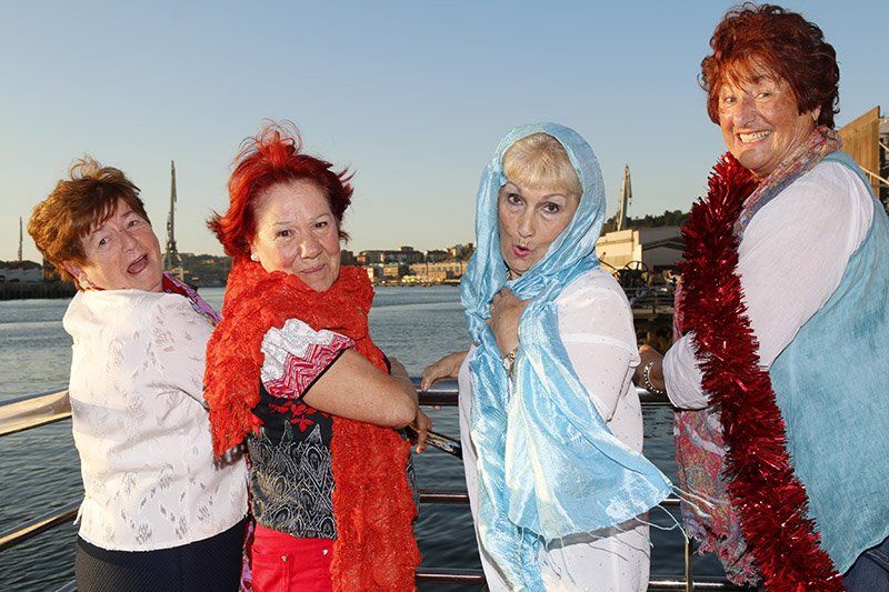 Cuatro mujeres en un bote. Una con pañuelo azul, las demás con pañuelo rojo y blanco. El río al fondo.