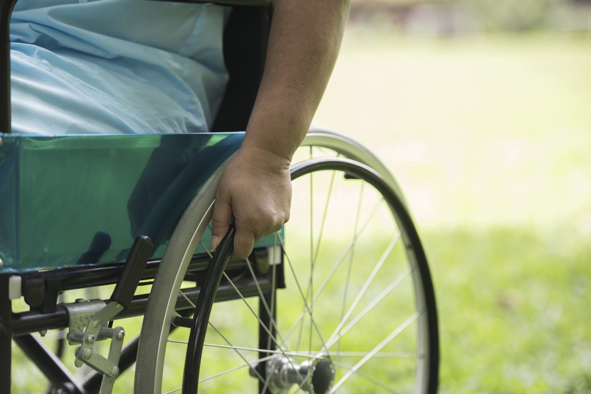 Persona en silla de ruedas, mano sobre volante al aire libre, césped verde al fondo.