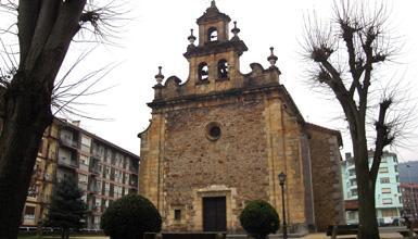 Una iglesia de piedra con un campanario y árboles circundantes en una plaza de la ciudad.