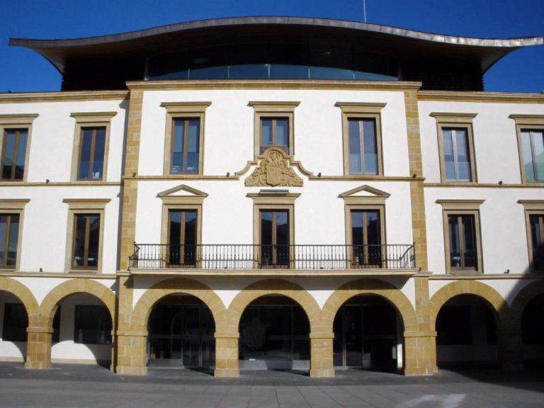 Edificio blanco con planta baja arqueada, balcones y techo curvo contra un cielo azul.