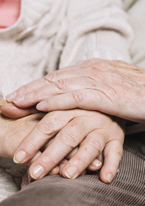 Primer plano de dos pares de manos ancianas unidas, apoyadas sobre una superficie marrón.
