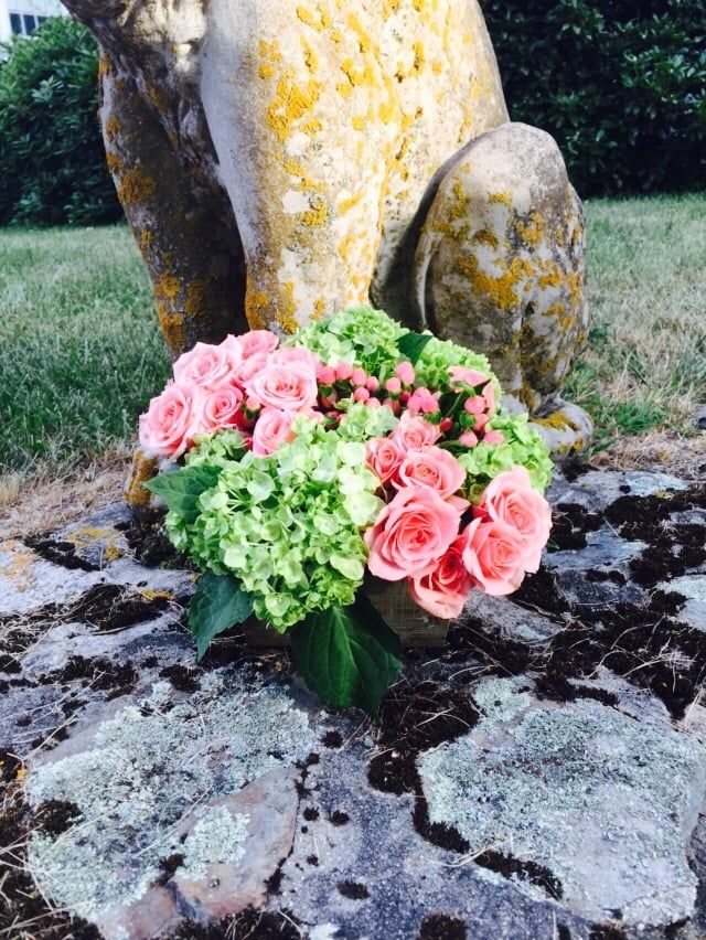 A bouquet of pink and green flowers is sitting on a rock in front of a statue.