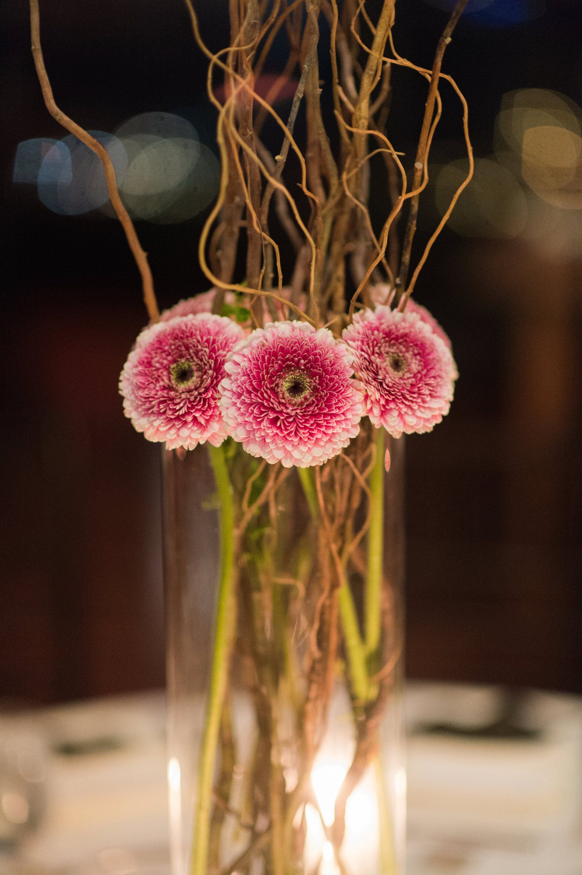 A vase filled with pink flowers and twigs on a table.
