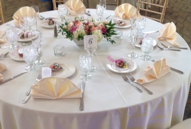 A table set for a wedding reception with plates , glasses , napkins and a vase of flowers.