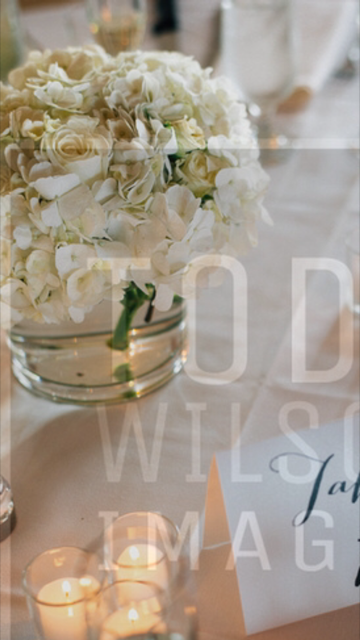 A vase filled with white flowers sits on a table next to candles.