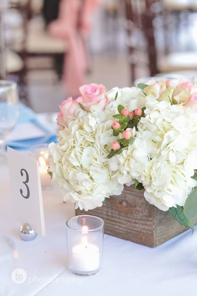 A wooden box filled with white flowers and pink roses is on a table.