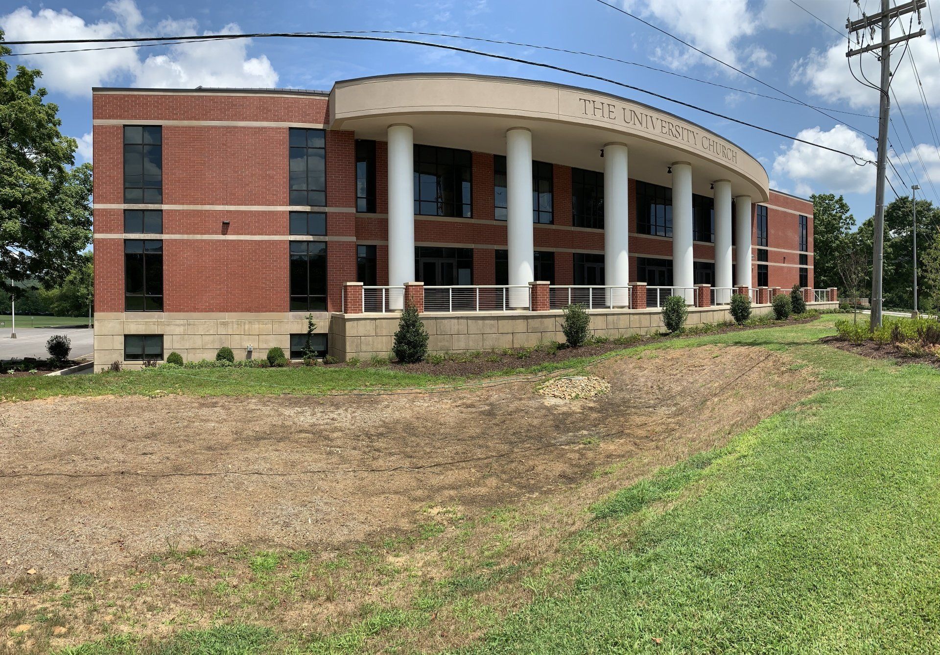A large brick building with columns is sitting in the middle of a grassy field.
