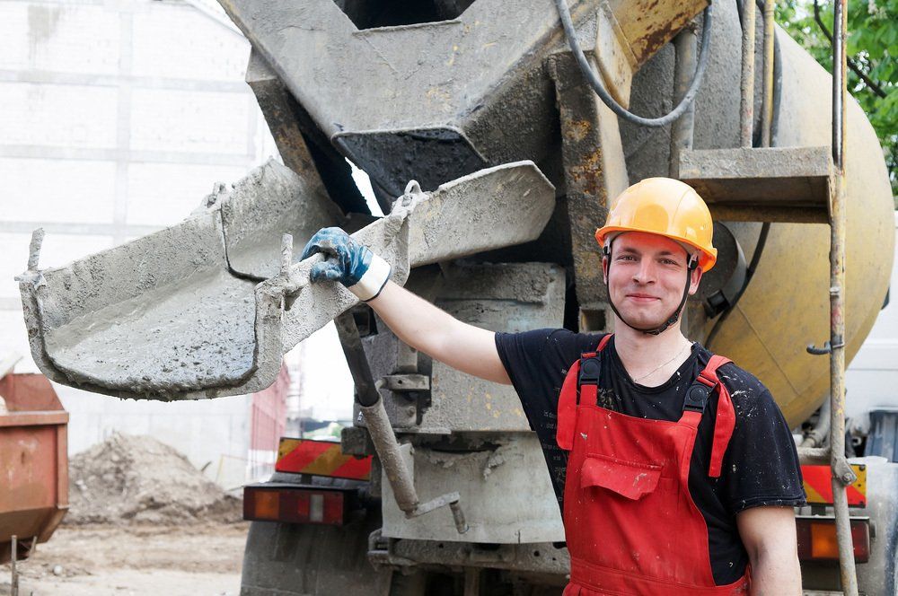 concrete contractor in hard hat and coveralls standing next to cement mixer truck