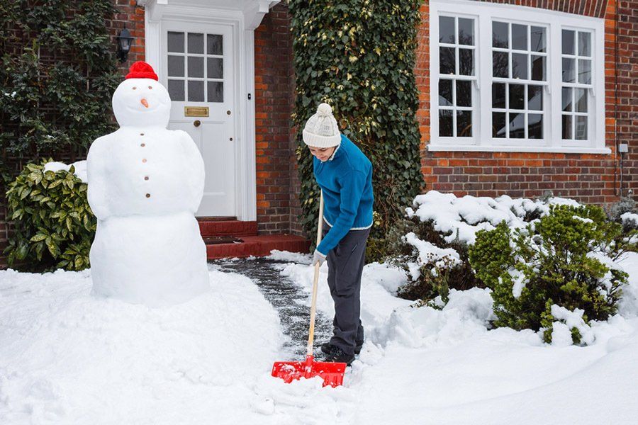 A man is shoveling snow in front of a snowman.