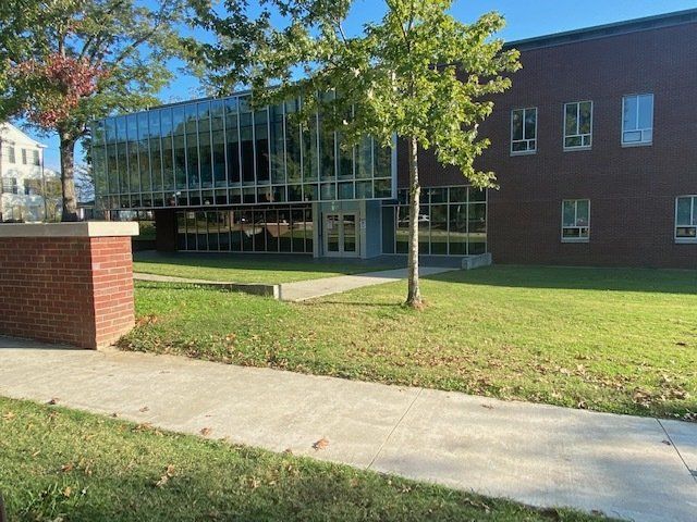 A modern building with a glass front, brick facade, and green lawn.