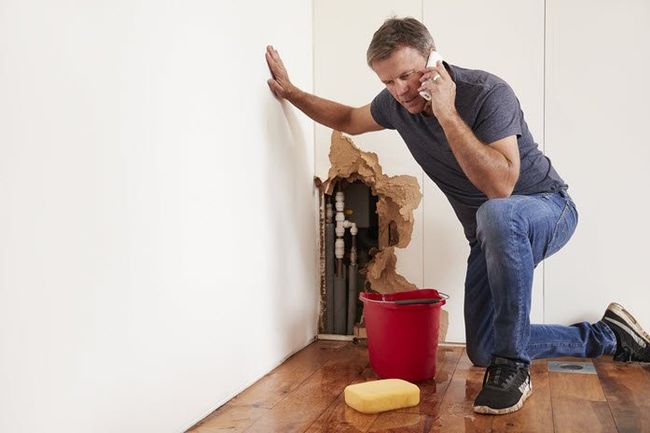 man using sponge to clean water from burst pipe