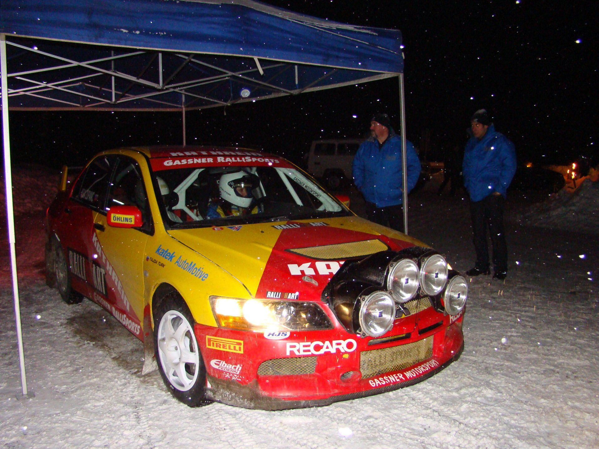 Startendes Rallye-Auto mit begeisterten Insassen in nächtlicher Winterkulisse.