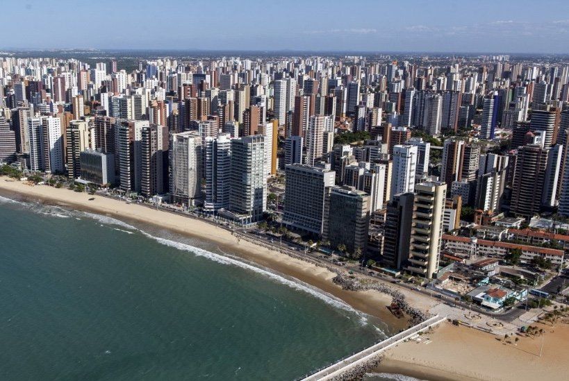 Aerial view of Fortaleza, Brazil, with skyscrapers lining a beach, and the ocean in front.