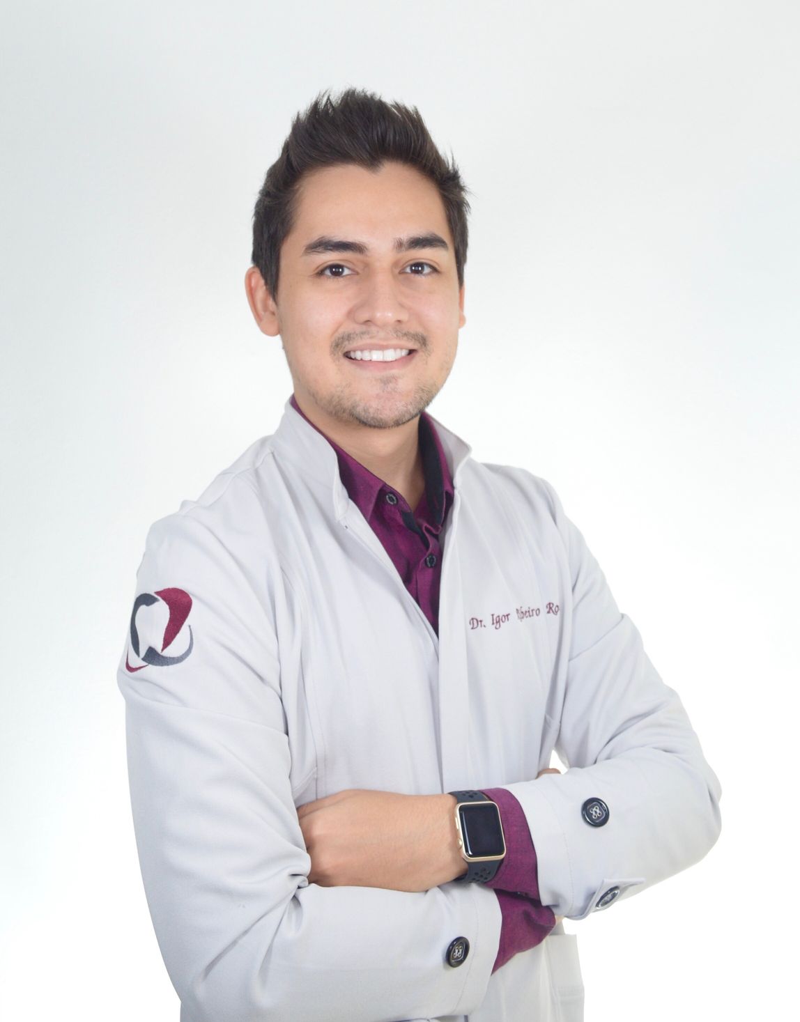 Uomo sorridente con camice bianco e braccia incrociate; logo della clinica odontoiatrica sulla manica.