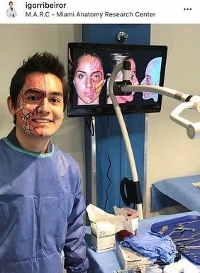 Un uomo con l'anatomia facciale esposta è in piedi in un laboratorio, su uno schermo viene visualizzata l'anatomia.