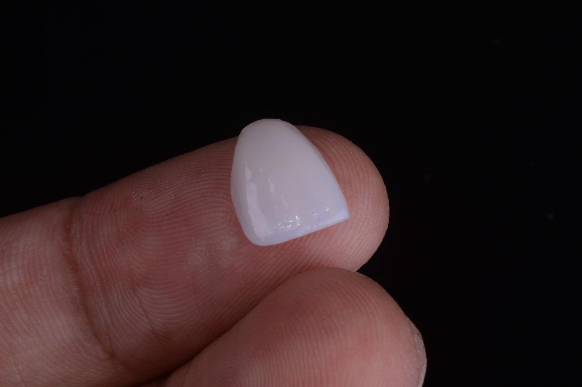 Una sola lámina de porcelana blanca sostenida entre dos dedos sobre un fondo negro.
