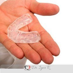 Protetor bucal transparente segurado na mão aberta de uma pessoa, contra um fundo branco.