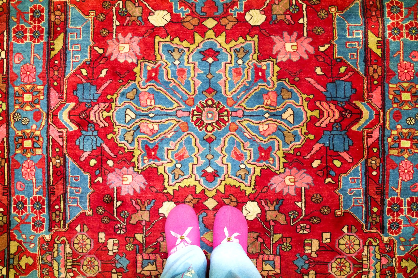 Bright red patterned rug with blue medallion and pink shoes at the bottom edge