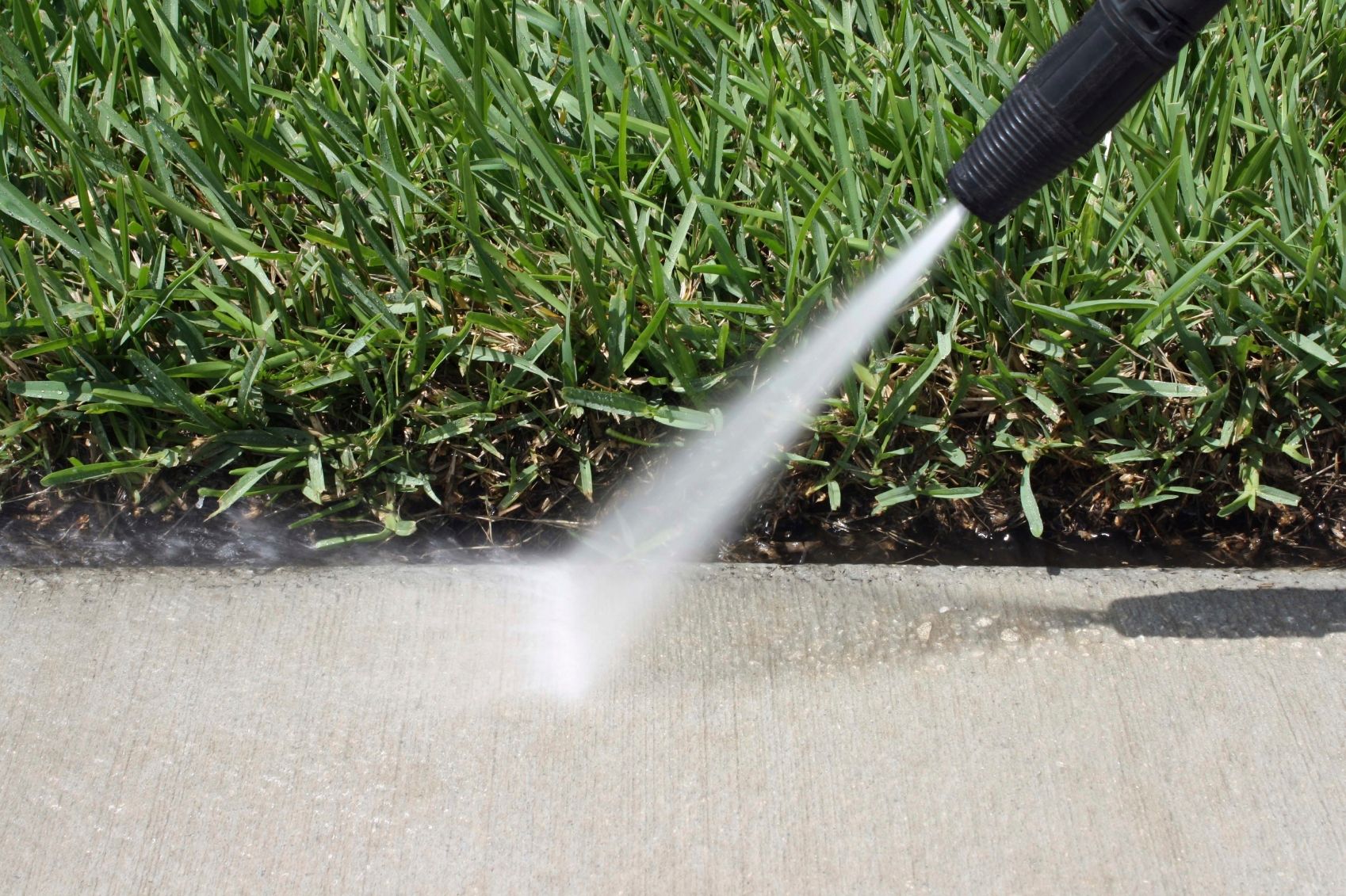 Water spraying from a hose onto a concrete sidewalk beside green grass