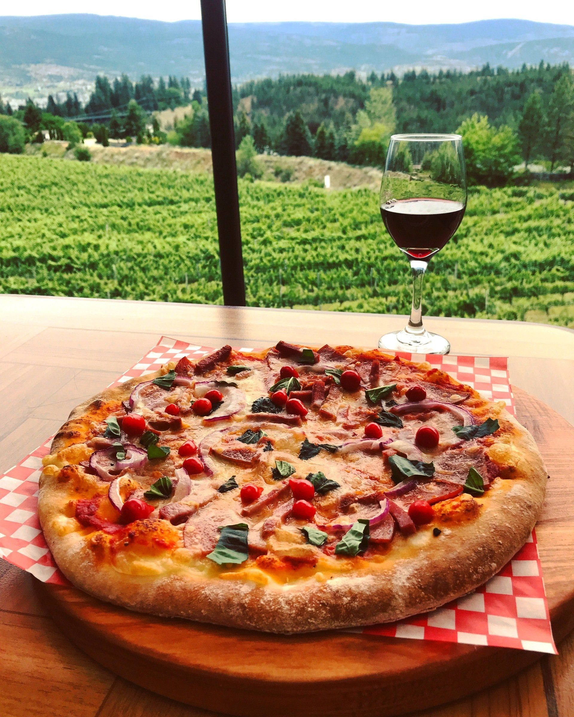 A pizza and a glass of wine on a table with a vineyard in the background