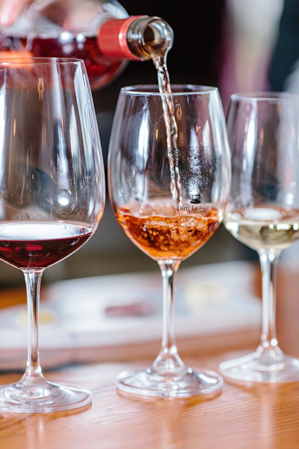 A person is pouring wine into three wine glasses on a table.