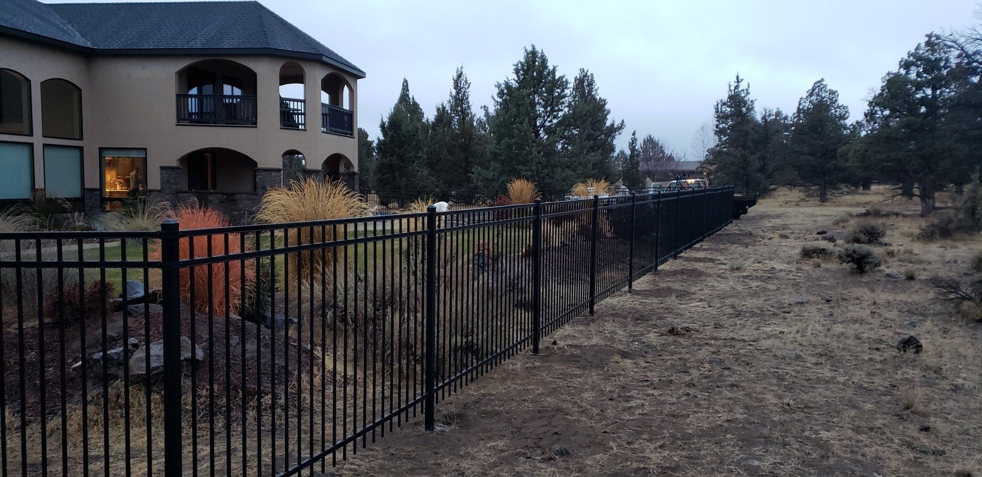 Black metal fence installed around residential property with soil ground