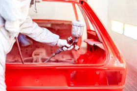 a man is spraying red paint on a red car